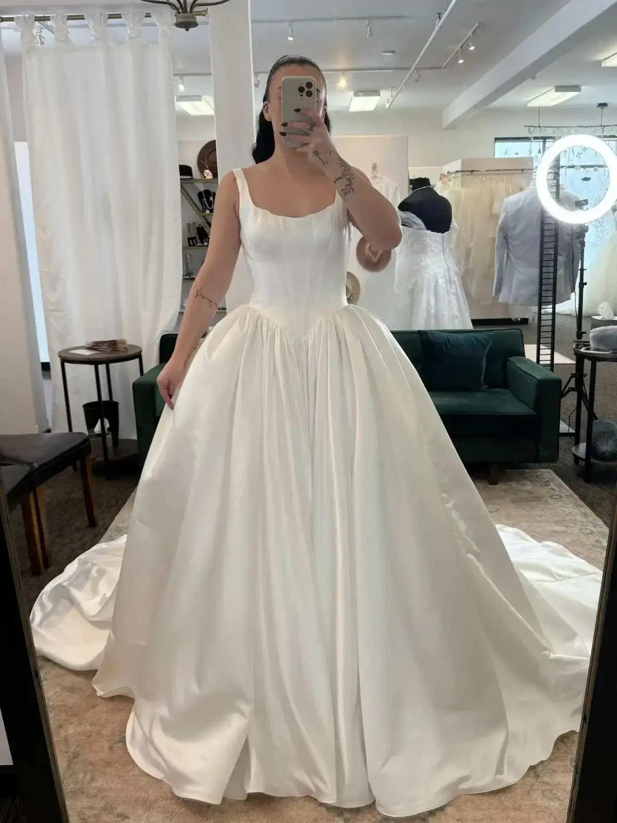 A person in a bridal shop wears a satin ball gown featuring a fitted bodice and voluminous skirt. The setting is elegant, with neutral-toned decor.